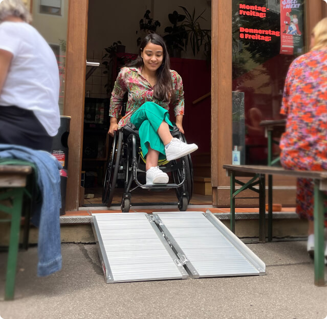 Frau im Rollstuhl fährt eine mobile Rampe herunter.